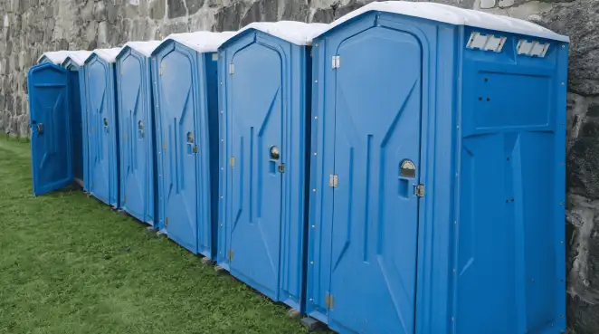 Row of blue portable toilets lined up on grass against a stone wall for event sanitation in Cleveland, OH