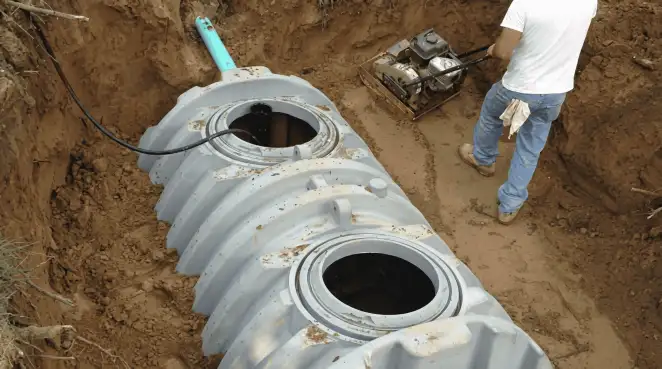 Septic tank installation showing a technician compacting soil around a new poly septic tank in an excavation pit in Cleveland, OH